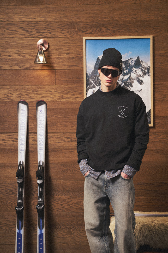 Man in ski attire standing next to skis against a wooden wall with a mountain scene.