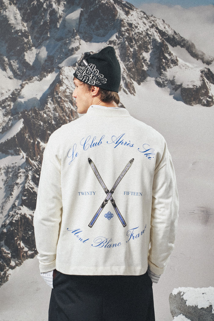 Person wearing a white long sleeved t-shirt with text and ski club logo against a snowy mountain background