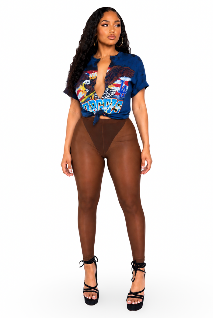 A woman modeling a two-piece outfit consisting of a blue short-sleeve graphic crop top with a plunging neckline and brown high-waisted sheer mesh leggings, paired with black lace-up platform heels, against a plain white background.