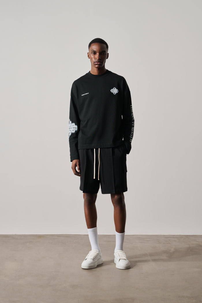 Person wearing a black long-sleeve t-shirt and shorts with white sneakers on a plain background