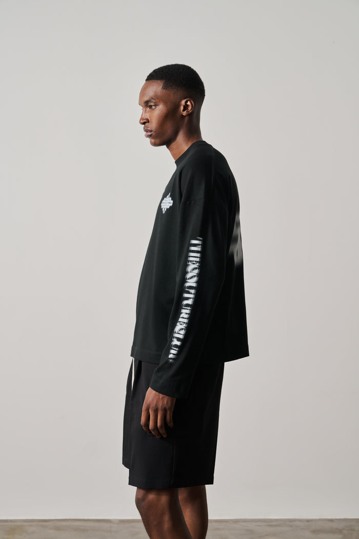 Man wearing a black long-sleeve t-shirt with white text on sleeves against a plain background