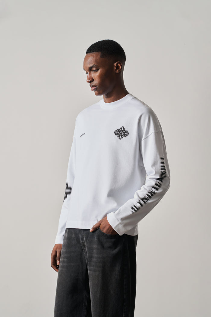 Man wearing a white long-sleeve t-shirt with black designs on a plain background