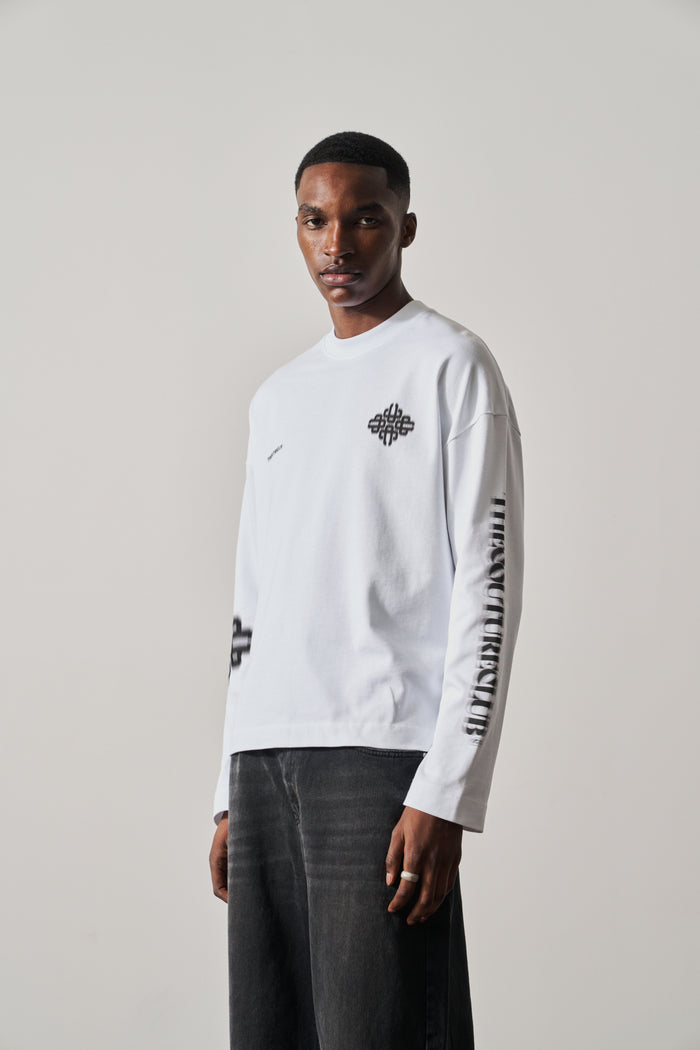 Man wearing a white long-sleeve t-shirt with black graphics on a plain background