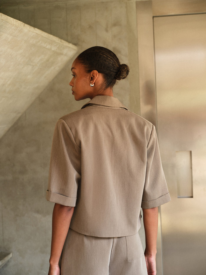 Woman wearing a beige outfit standing in a room with neutral walls.